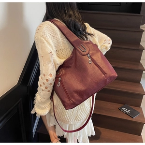 Rear view of model holding a burgundy pebbled leather tote bag on wooden stairs