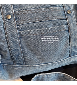 Detailed macro view of denim fabric with orange stitching and silver rivets on a crossbody bag