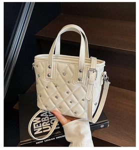 Detail of cream quilted bucket bag with silver studs on a modern urban background