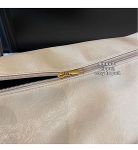 Close-up of smooth gold metal zipper and leather texture on a cream tote bag