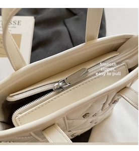 Detail of smooth metal zipper and diamond quilted texture on off-white bucket bag