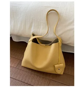 Dettaglio borsa tote gialla in pelle con ciondolo a cuore su letto bianco