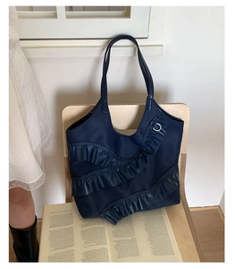 Detail of navy blue nylon tote bag with layered leather ruffles on wooden chair