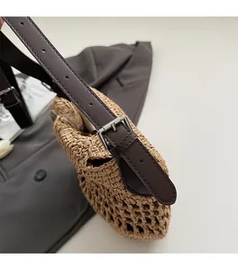 Detailed view of dark brown leather strap with silver buckle on woven straw shoulder bag