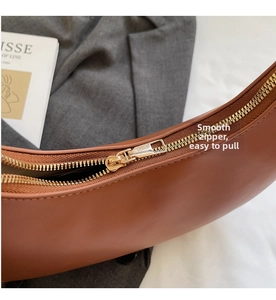 Close-up of golden zipper detail on brown leather crescent shoulder bag with fine stitching
