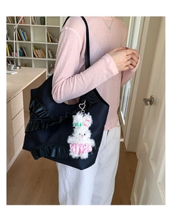 Detail of black tote bag featuring lace ruffles and a white plush bunny charm attachment