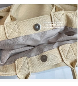 Detalle de hebilla magnética plateada y cuero granulado en un bolso tote crema