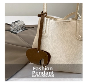 Détail du charm de sac en forme d'éléphant en cuir marron sur un sac à main blanc cassé