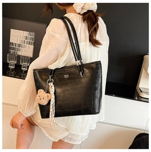 Détail d'un grand sac cabas noir à motif crocodile avec breloque ours et ruban déco