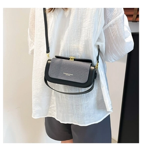 Detail of elegant black leather crossbody bag with woven texture flap and gold clasp
