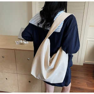 Minimalist beige soft leather tote bag shown on shoulder in a cozy indoor setting