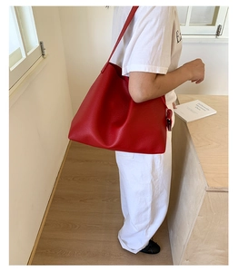 Dettaglio borsa tote rossa in pelle martellata con pendente laterale indossata da modella