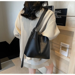 Detail of black lychee grain leather bucket bag with wide strap on a female model