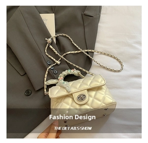 Close-up of cream quilted bag with metal twist lock, chain strap, and silk scarf handle