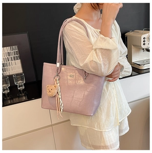 Détail du sac cabas violet gaufré croco avec breloque ours et foulard sur l'épaule du mannequin