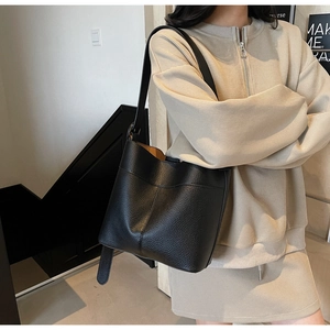 Side view of a black lychee texture leather bucket bag worn by a model in interior