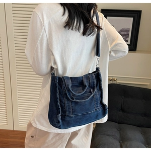 Model view of a vintage dark blue denim crossbody tote bag with adjustable shoulder strap