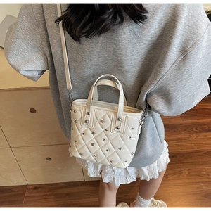 Detail view of a white quilted bucket bag with silver studs worn by a model