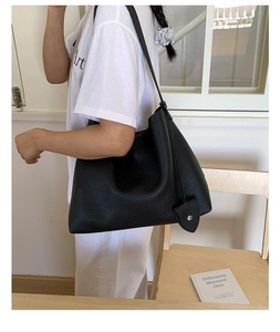 Vista laterale della borsa tote in pelle nera a grana fine con tracolla e ciondolo