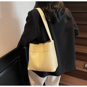 Detail of light yellow bucket bag in lychee pattern leather styled on a model's shoulder