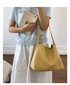 Dettaglio di una grande borsa tote gialla in pelle indossata da una modella in stile minimal