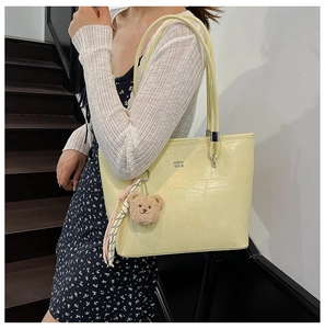 Details der hellgelben Totebag mit Krokoprägung, Teddybär-Anhänger und silbernen Beschlägen