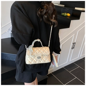 Close-up of white quilted crossbody bag featuring chain strap and woven top handle detail