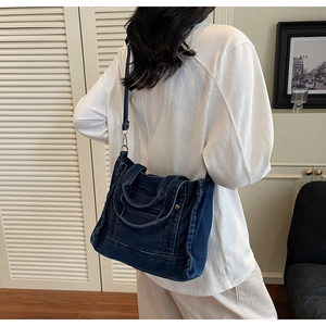 Detailed view of dark blue denim crossbody bag featuring metal buckles and stitching