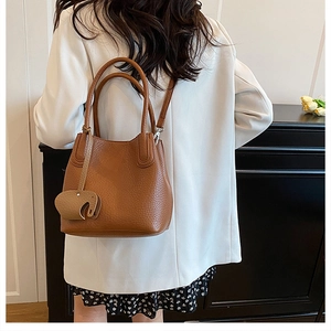 Détail d'un sac seau marron à motif litchi avec un charmant pendentif en cuir éléphant