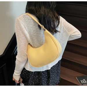 Pale yellow crescent-shaped shoulder bag made of fine leather in a casual outdoor setting