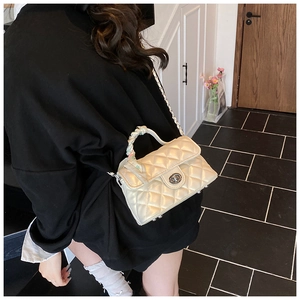 Detail of quilted crossbody bag with gold chain strap and silk handle on model