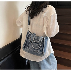 Detail of blue denim crossbody bag featuring metal rivets and detachable shoulder strap