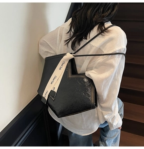 Detail of glossy black heart-shaped shoulder bag with printed ribbon and textured finish
