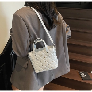 Detailed back view of a white quilted bucket bag with silver studs worn cross-body