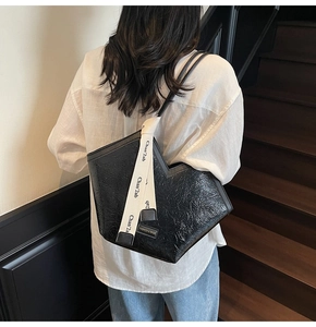 Detail of black pleated patent leather tote bag showing texture and branding on a model