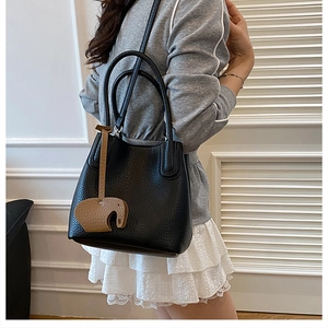 Gros plan d'un sac seau en cuir noir avec breloque éléphant porté par un mannequin