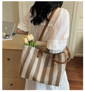 Woman wearing a large striped straw tote bag with brown leather straps in a cozy room