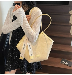 Detail of cream pleated leather shoulder bag with decorative ribbon and logo label