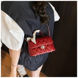 Detail of red quilted crossbody bag with metal chain strap and decorative silk scarf handle