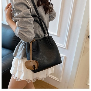 Détail d'un sac seau en cuir grainé noir avec un accessoire charm éléphant marron