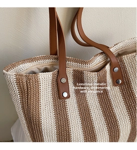 Macro shot of striped straw tote bag showing brown leather straps and metal rivet detail