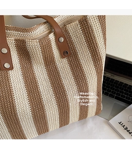 Detail of woven straw tote bag with brown leather handles and vertical stripe pattern