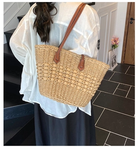 Detail of woven straw tote bag featuring brown leather shoulder straps and reinforced stitching