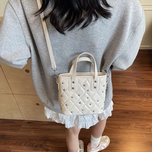 Chic beige quilted bucket bag with silver studs worn by a model in a cozy setting
