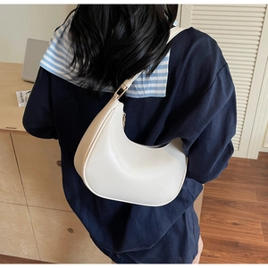 Detail of a minimalist cream crescent shoulder bag worn with a stylish navy outfit