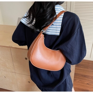Brown moon-shaped underarm bag shown in a lifestyle shot with a model and soft lighting