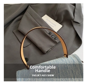 Detail of light blue denim handbag featuring a dark brown leather curved handle and texture