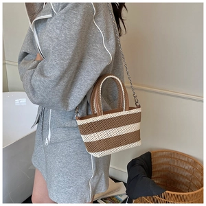 Detailed view of woven striped tote bag with metal chain strap and brown handles on a model