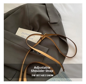 Detail of adjustable brown leather shoulder strap with metal buckle on a gray blazer