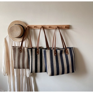 Detail view of woven straw tote bags with leather handles hanging in a lifestyle setting